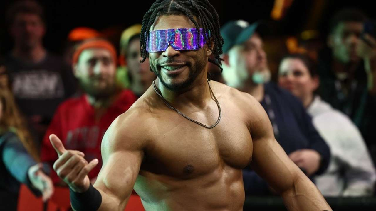 Kevin Knight realiza su entrada al ring durante un evento de AEW mientras saluda al público con sus característicos lentes de sol de colores.