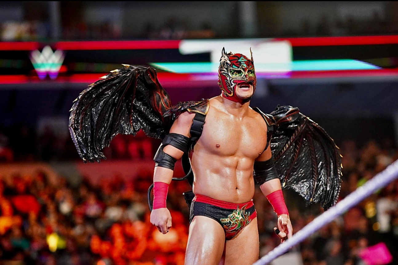 Dragon Lee realiza su entrada al ring con una máscara roja y negra y un impresionante atuendo con alas negras durante un evento de WWE.