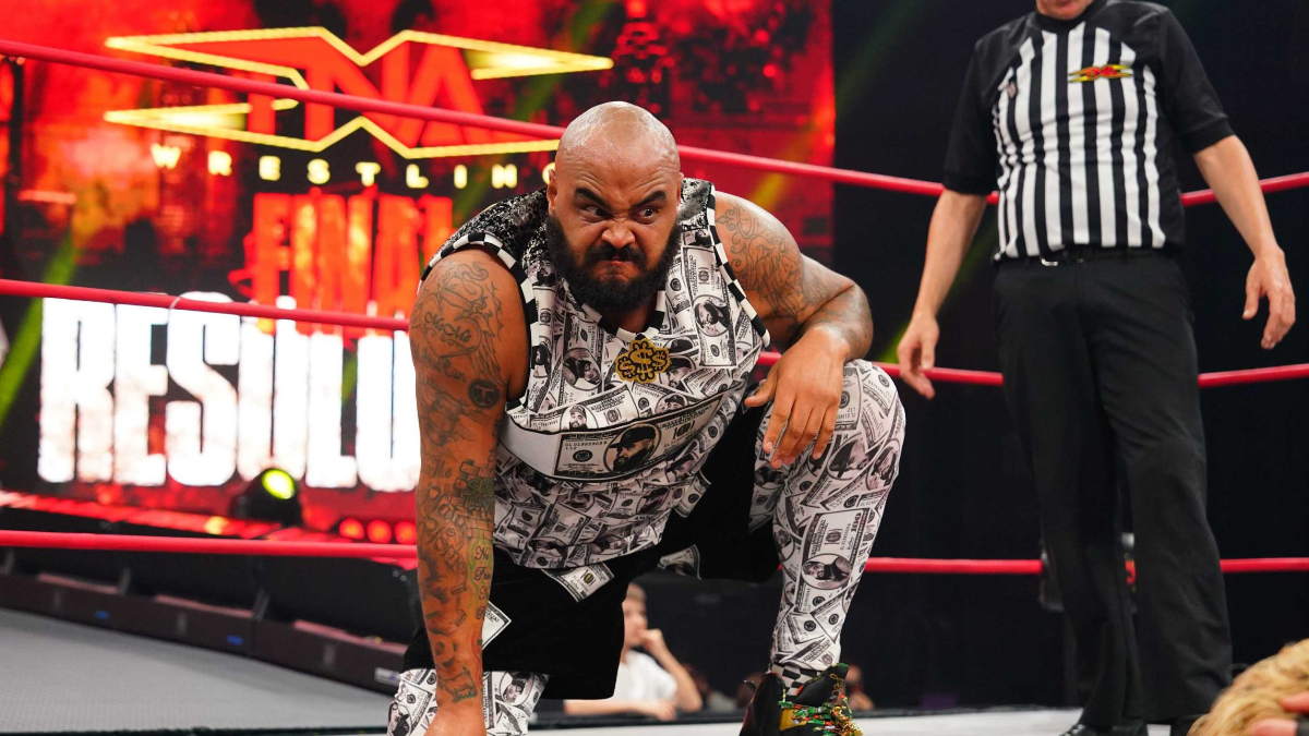 AJ Francis con una rodilla sobre la lona y vestimenta con estampado de billetes en el ring de TNA Wrestling.