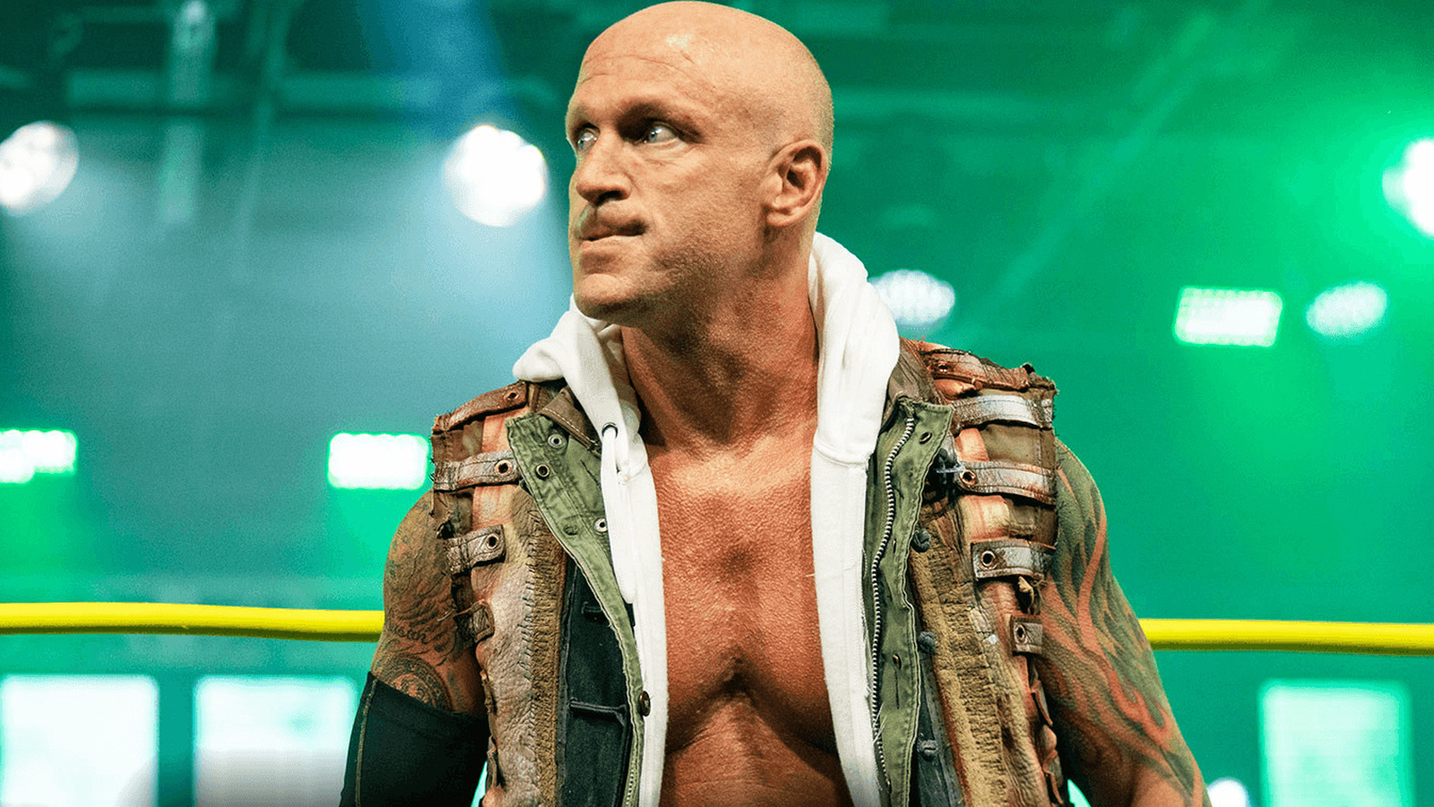 Eric Young en el ring de TNA Wrestling, con un chaleco marrón y una capucha blanca bajo luces verdes.